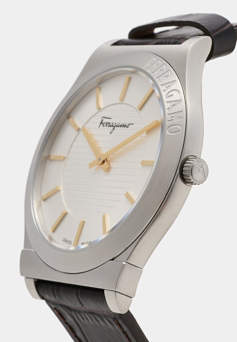 Montre argentée Ferragamo avec cadran blanc, marquage et aiguilles dorées, bracelet en cuir marron, et Ferragamo gravé sur la lunette.