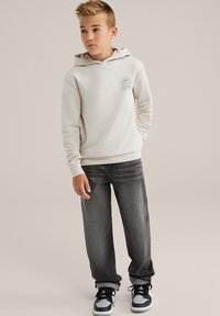  Lichtbeige hoodie met een zonafbeelding, gecombineerd met grijze denim jeans en zwarte sneakers met witte accenten.