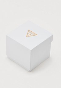 Caja de regalo cuadrada blanca con superficie texturizada y logo triangular dorado en la tapa, que incluye el nombre de la marca "GUESS" y detalles del producto.