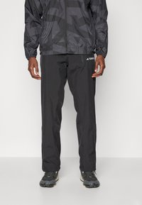 Schwarze wasserdichte Jacke mit geometrischem Muster, Reißverschluss und elastischen Bündchen, kombiniert mit passenden schwarzen wasserdichten Hosen und Outdoor-Schuhen.