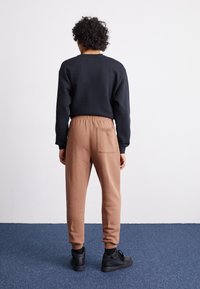 Black sweatshirt and brown sweatpants with side pocket, elastic waistband, and tapered ankles. Worn with black sneakers. Neutral background.