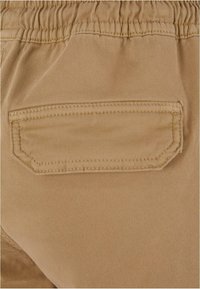Gros plan sur un tissu beige avec une ceinture élastique et une poche arrière rectangulaire à double surpiqûre.