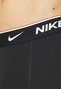 Fekete Nike boxer alsónadrág széles elasztikus derékkal, melyen fehér Nike logó és varrási részletek láthatók. Az anyag simának és testhezállónak tűnik.