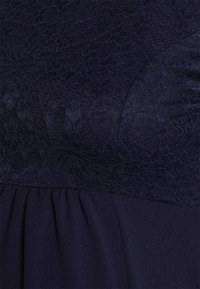 Vestido azul-marinho com corpete de renda texturizada com padrão floral e parte inferior lisa e pregueada, criando uma silhueta estruturada.