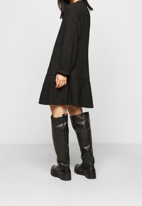 Černé dlouhé šaty s texturovanou tkaninou, s volánovým lemem. Zkombinováno s vysokými, lesklými černými kozačkami po kolena.