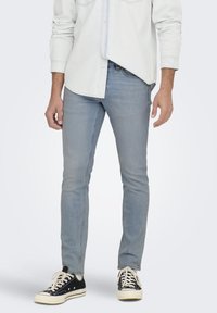 Jeans de mezclilla azul claro con un ajuste slim, que presentan una textura suave y un ligero desgaste, combinados con zapatillas bajas negras.