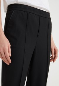 Svarta byxor med plisserad front, elastiskt midjeband och sidfickor. Slät tygkvalitet med en skräddarsydd passform och inga synliga mönster.