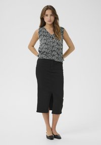 Jupe noire mi-longue avec une fente à l'avant, associée à un top sans manches avec un motif à rayures verticales noir et blanc. Texture de tissu lisse.