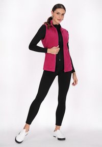 Vest din fleece de culoare roz vibrant, cu un design ajustat, guler înalt și fermoar frontal. Purtați peste un top negru cu mânecă lungă și asortați cu colanți negri.