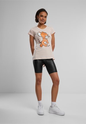 Ljusrosa t-shirt med en tecknad musgrafik i orange på framsidan, kombinerad med svarta fusk lädershorts och vita sneakers.