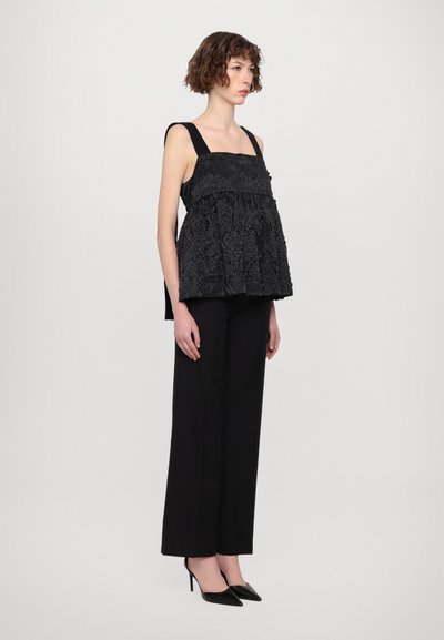 Top texturat floral negru cu bretele groase, design stratificat, purtat peste pantaloni largi negri; model în poziție laterală.