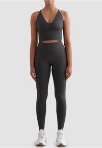 Szary sportowy biustonosz z wycięciem, w połączeniu z pasującymi legginsami z wysokim stanem, oba wykonane z teksturowanego, elastycznego materiału. Białe trampki.