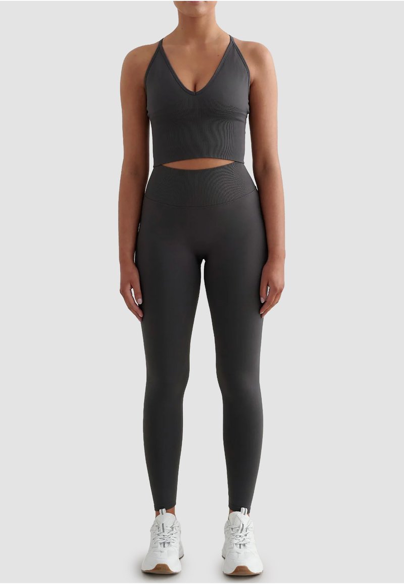 Szary sportowy biustonosz z wycięciem, w połączeniu z pasującymi legginsami z wysokim stanem, oba wykonane z teksturowanego, elastycznego materiału. Białe trampki.