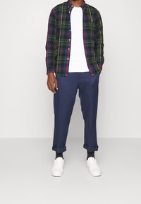 Koszula flanelowa w kratkę w kolorach zielonym, granatowym, czerwonym i żółtym, nałożona na biały t-shirt; w połączeniu z granatowymi spodniami z lekko podwiniętymi nogawkami i białymi trampkami.