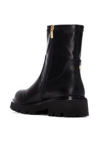 Bota de ankle de cuero negra con cremallera lateral y detalles en hardware dorado. Suela gruesa con un patrón texturizado para mayor agarre. Acabado de superficie suave.