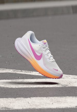 Fehér Nike futócipő rózsaszín logóval és narancssárga talppal, szürke járdán, fehér vonalakkal lebegve.