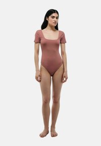 Body côtelé de couleur rose poussiéreux, avec un décolleté carré et des manches courtes, fabriqué dans un tissu extensible, avec une silhouette ajustée.