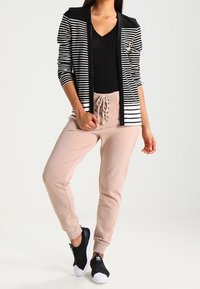 Cárdigan ligero a rayas blancas y negras con un diseño ajustado, sobre una camiseta negra con escote en V, combinado con pantalones jogger rosa claro y zapatillas negras.