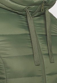 Chaleco acolchado verde con cuello alto, textura suave, cremallera frontal y cuerdas ajustables. Presenta costuras horizontales.