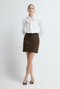 Witte blouse met strikdetail, bruine textuurrijke minirok en zwarte slingback hakken met gouden accenten. Eenvoudig en modern ontwerp.