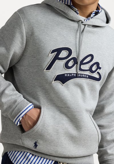Felpa grigia con un grande logo navy di "Polo Ralph Lauren". Presenta una tasca frontale, cappuccio con cordino, e una maglietta a righe visibile sotto.