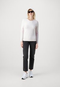 Lyserød langærmet top i kombination med sorte jeans og hvide sneakers. Tilbehøret inkluderer solbriller og en hvid kasket. Enkel design og neutrale farver.