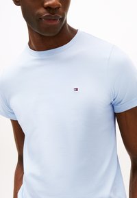 Šviesiai mėlynas medvilninis marškinėlis su apvalia iškirpte ir trumpomis rankovėmis. Ant krūtinės yra mažas raudonas, baltas ir mėlynas siuvinėtas logotipas.