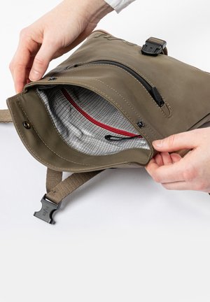 Olivengroene tas met een ritssluiting, voorzien van een gestreepte grijze binnenkant en een rode accentzoom. Inclusief een stoffen riem en een plastic gesp.