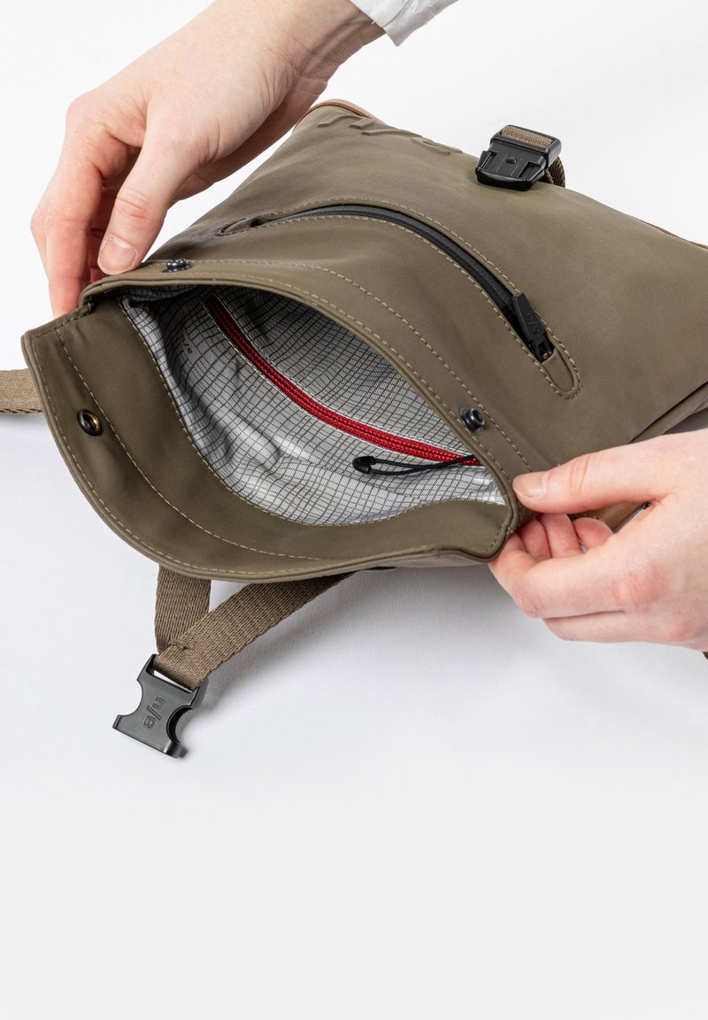 Zaino verde oliva con apertura con zip. L'interno presenta un motivo a griglia grigia e dettagli rossi. Include un gancio nero e una tracolla regolabile.