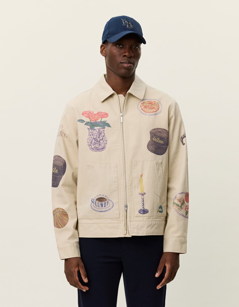 Μπεζ μπουφάν με διάφορες εκτυπωμένες εικονογραφήσεις, περιλαμβανομένων λουλουδιών, τροφών και ενός κεριού, με δύο μπροστινές τσέπες.