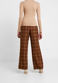 Top lungo a maniche lunghe rigato beige abbinato a pantaloni larghi a quadri marroni con un motivo a plaid crema e sandali open-toe.