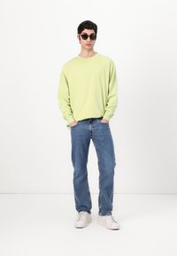 Light green long-sleeve shirt with a crew neckline, paired with blue straight-leg jeans and white sneakers. Accessories include black sunglasses.