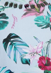 Tkanina w kwiatowy wzór z zielonymi liśćmi i różowymi kwiatami, ozdobiona srebrnymi i fioletowymi kamieniami wzdłuż górnej krawędzi. Jasny kolor tła.