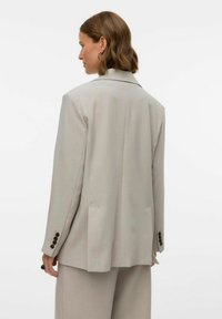 Vaaleanharmaa bleiseri, jossa on muotoiltu istuvuus, strukturoidut olkapäät ja kaksi takaventtiä. Varustettu napitettavilla hihansuilla ja minimalistisella suunnittelulla.