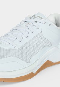 Λευκό αθλητικό παπούτσι με πλέγμα πλευρικής όψης, λευκά κορδόνια, επενδυμένο γιακά και ταμπά καουτσούκ σόλα, εμφανιζόμενο σε κοντινή γωνιακή όψη.