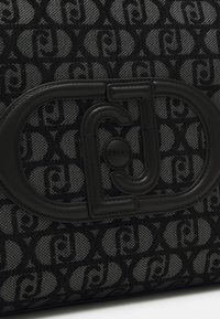 Borsa nera con texture che presenta un motivo a logo e un accent circolare in pelle nera molto evidente. Il materiale combina tessuto e pelle liscia.