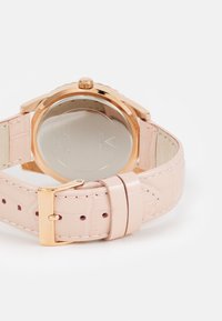 Runde Uhr mit einem reflektierenden silberfarbenen Gehäuseboden, pinkfarbenem Krokodillederarmband und goldfarbenen Beschlägen, ausgestattet mit einer Schnallenverschluss.