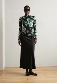 Lange zwarte satijnen rok gecombineerd met een aansluitend coltrui-top met een groen en wit bloemenpatroon. Inclusief zwarte zonnebril en platte schoenen.