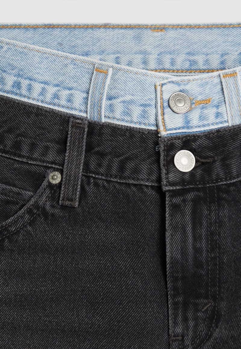 Jeans en denim noir avec une taille bleu clair. Équipés de quincaillerie argentée, de surpiqûres orange et d'une texture lisse. Boutons à la taille.