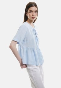Blusa azzurra a maniche corte con scollatura rotonda, dettaglio con fiocco davanti e design a peplum svasato. Tessuto liscio e testurizzato.