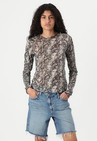 Haut à manches longues avec un imprimé serpent dans des nuances de marron et de beige, en tissu texturé, associé à un short en jean bleu clair avec des bords effilochés.