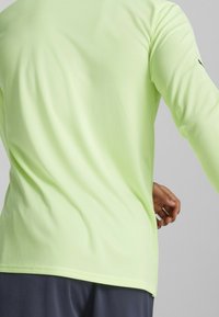 Langærmet atletisk skjorte i lys limegrøn, struktureret stof, tætsiddende design, afrundet kant, med en lille logo på ærmet.
