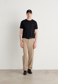 Tricou negru cu mânecă scurtă și logo, pantaloni bej drepti, curea neagră și adidași negri, purtat cu o șapcă neagră. O ținută simplă și coerentă.
