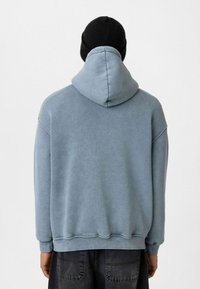 Lichtblauwe hoodiesweater met een relaxte pasvorm, ribgebreide mouwen en een gladde textuur, gecombineerd met een zwarte gebreide beanie.