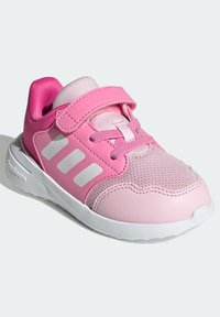 Chaussure de sport rose avec tige en maille, accents synthétiques, design à trois bandes blanches, bride velcro et semelle rembourrée pour le confort.