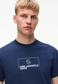 Navyblauwe katoenen t-shirt met korte mouwen, met een witte geprinte logo en de tekst "KARL LAGERFELD JEANS" in een rechthoekig ontwerp op de voorkant.