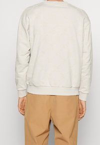 Sweat-shirt taupe clair avec motif texturé, poignets et ourlet côtelés. Col rond. Associé à un pantalon beige.