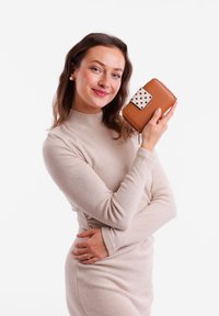 Brown leather wallet with a white polka dot accent and a zip closure, held by a person wearing a light beige sweater in a plain background.