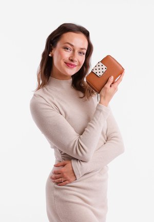 Brown leather wallet with a white polka dot accent and a zip closure, held by a person wearing a light beige sweater in a plain background.