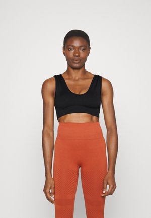 Top cropped preto com decote arredondado e alças largas, combinado com leggings laranja de cintura alta que apresentam padrões diagonais texturizados.